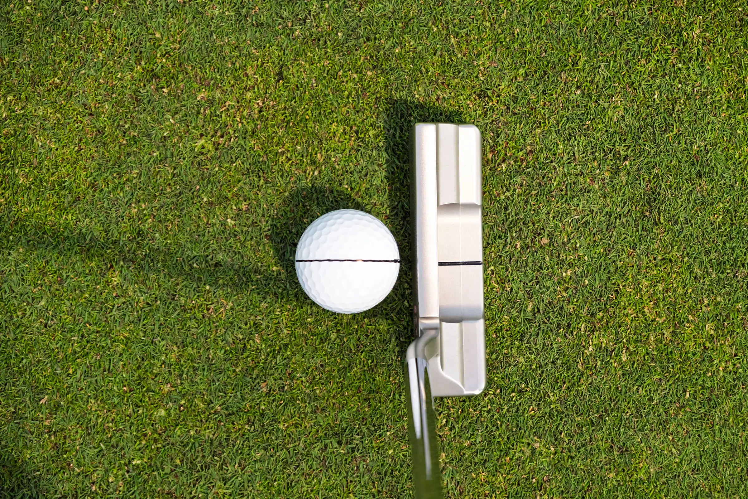 Overhead view of a golf ball and putter alignment line on the green, showing putting setup, aim and stroke accuracy practice.