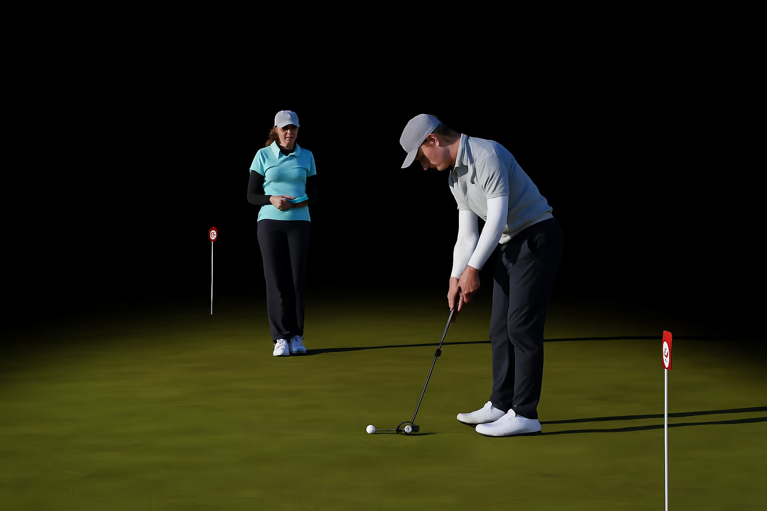 Two golfers on a putting green using a Capto putting analysis device, with one player preparing to putt while the other observes and records data.