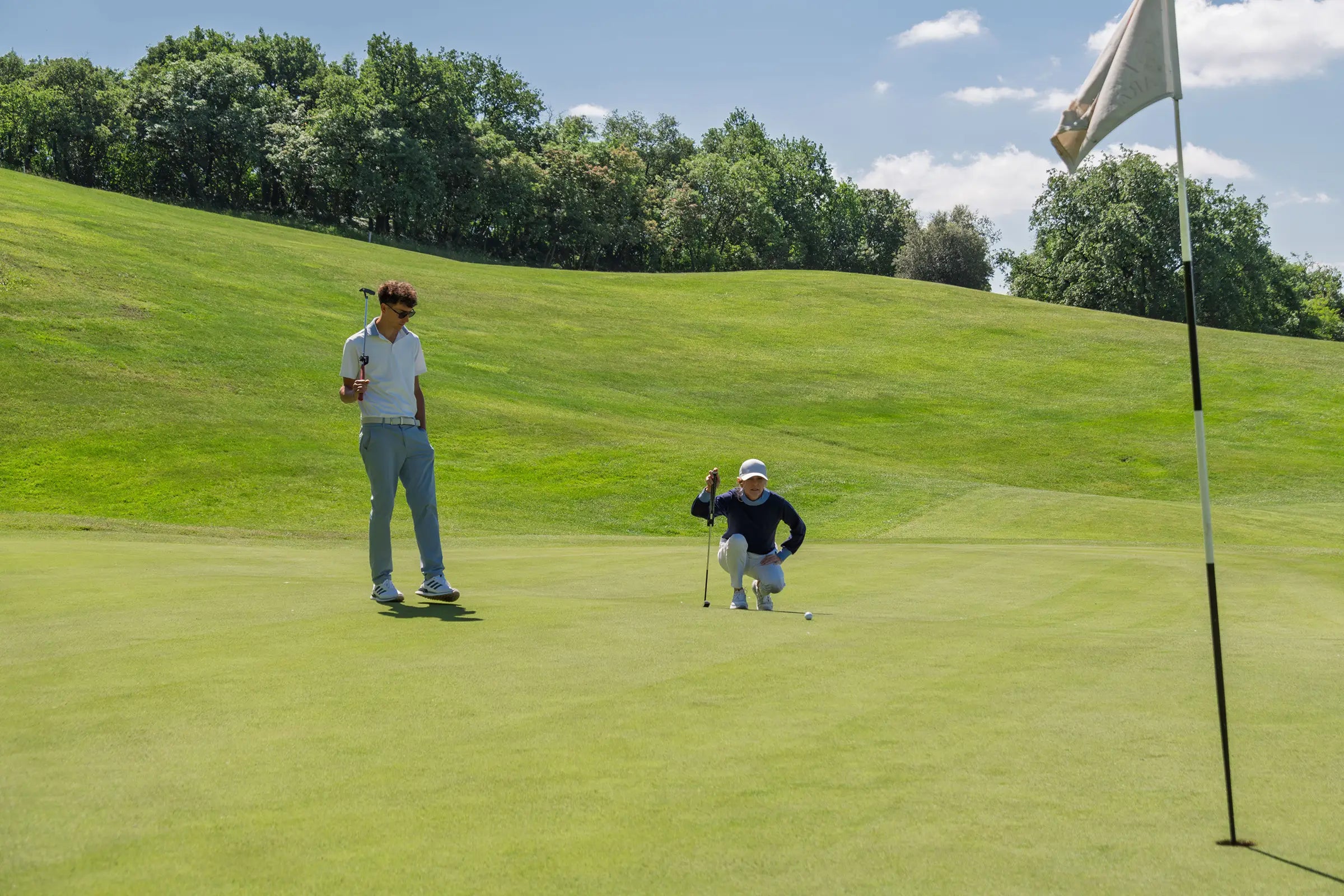 Golfer in white putting on green using Capto Gen 3 while coach watches on a sunny golf course.